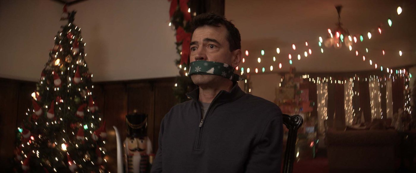 Mark, gagged with a Christmas napkin, in the Kringles' living room